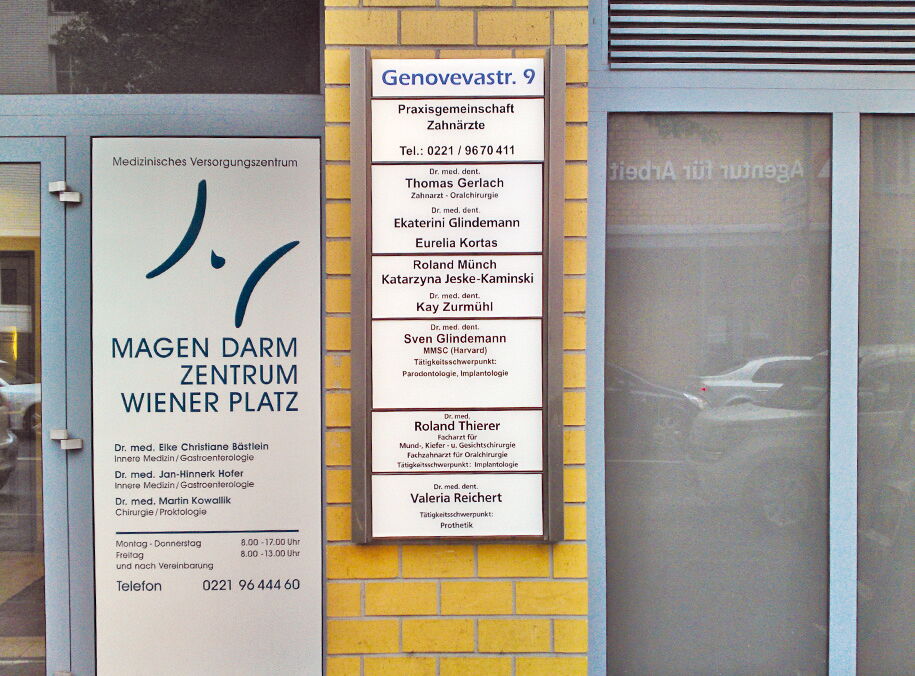 Beleuchtetes Praxisschild mit Namensliste am Eingang eines Gebäudes